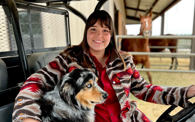Abby driving a side by side while petting her dog. Horses are in the background.